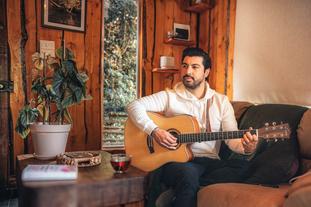Persona tocando guitarra sentada en un sillon en una casa estilo rustico